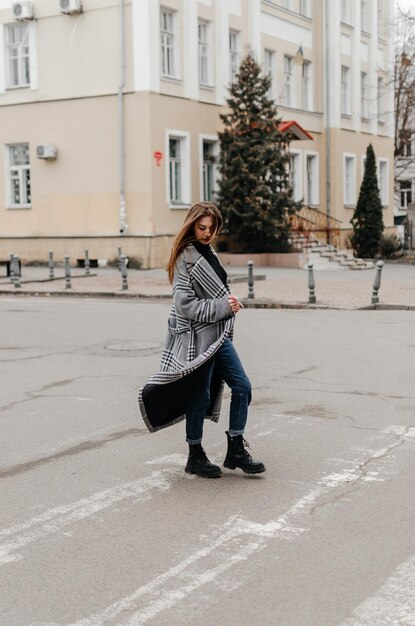 Женщина переходит улицу в пальто и джинсах