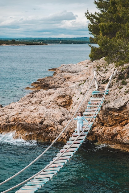 Woman crossing suspension bridge sea on background