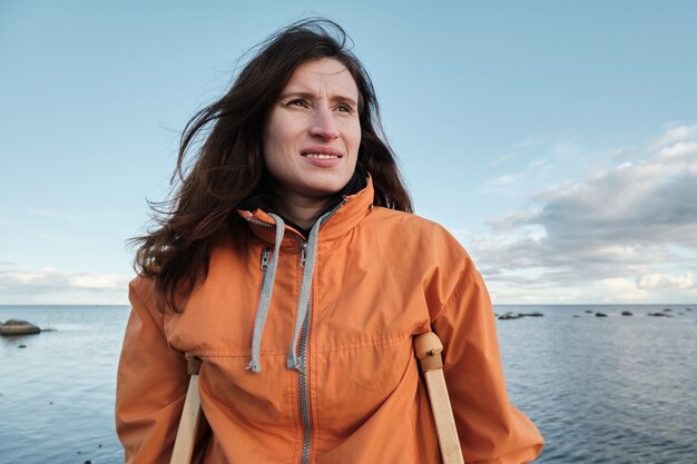 A woman on crutches walks along the shore of the lake.