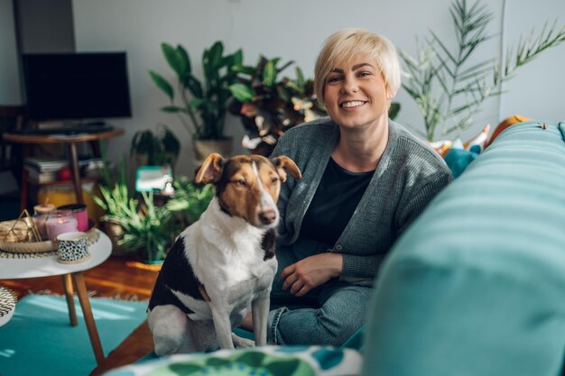 Женщина обнимается и играет со своей собакой дома на диване
