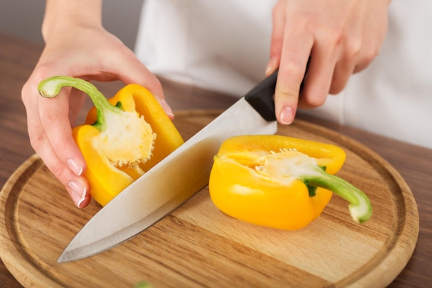 Woman cut yellow bell peppers on table background