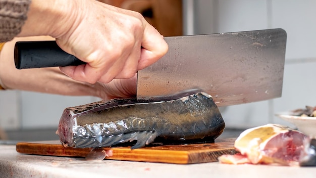 A woman cuts fish with a large knife at home in the kitchen