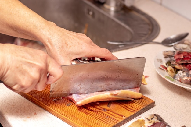 女性が自宅のキッチンで大きな包丁で魚を切る