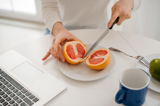 Woman cuts a grapefruit with a knife closeup view