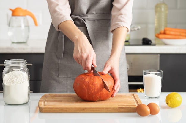 A woman cuts a pumpkin to make a pie in her kitchen