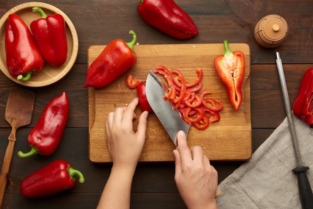 Woman cuts red bell pepper into pieces on wooden board