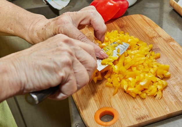 Woman cuts red and yellow bell peppers for cooking at home using recipe from the Internet. Preparation of ingredients and vegetables before cooking.