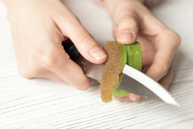 Photo woman cuts ripe kiwi fruit, close-up