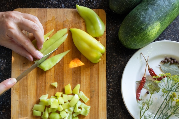 A woman cuts a sweet pepper on a wooden board to prepare a vegetable salad for the winter Female hands with a knife flat lay