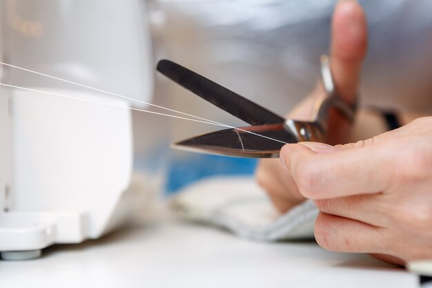 Woman cuts thread with scissors in sewing machine