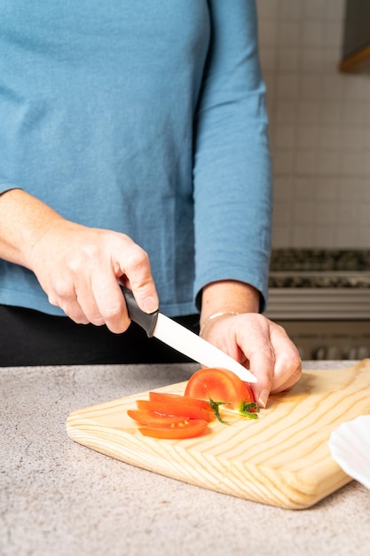 사진 여자는 집에 있는 부엌에서 나무 판자에 토마토를 자른다