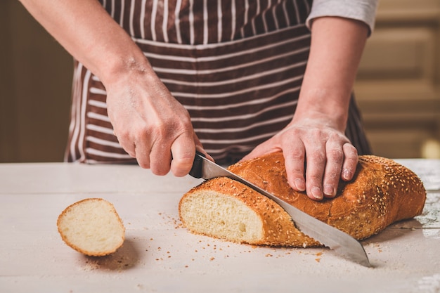 Pane di taglio della donna sulla tavola di legno. forno. produzione di pane. una donna con un grembiule a righe