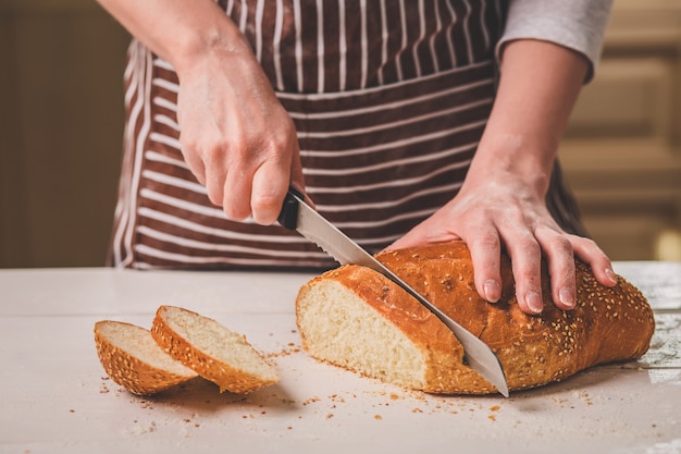 Woman cutting bread on wooden board. Bakehouse. Bread production. A woman in a striped apron