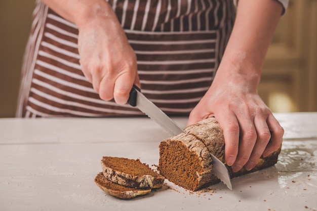 Woman cutting bread on wooden board. Bakehouse. Bread production. A woman in a striped apron