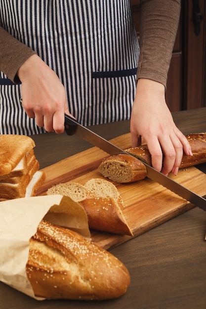 Woman cutting bread on wooden board. Unrecognizable female chef preparing healthy sandwiches, side view, copy space