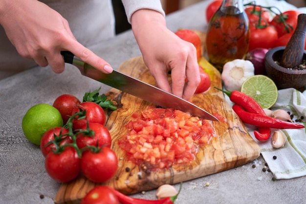 Woman cutting and chopping blanched tomato by knife on wooden board