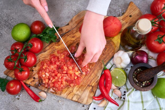 Woman cutting and chopping blanched tomato by knife on wooden board