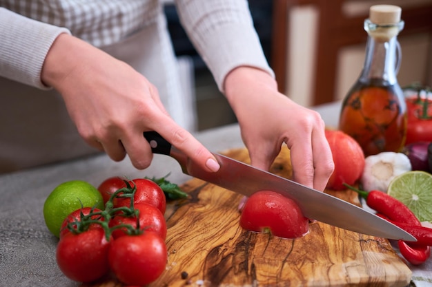 Woman cutting and chopping blanched tomato by knife on wooden board