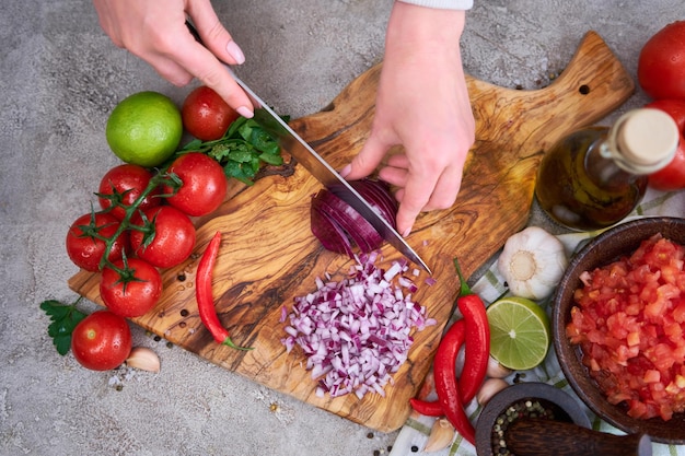 Woman cutting and chopping onion by knife on wooden board