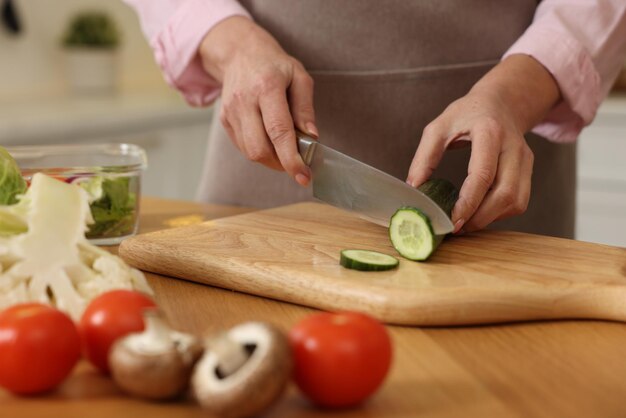 Woman cutting cucumber at wooden table in kitchen closeup