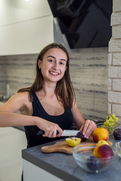 woman cutting different fruits cooking healthy food on a kitchen wood table