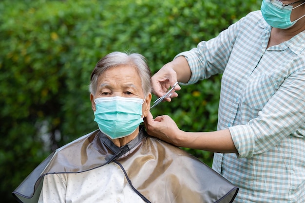 Woman cutting female senior hair during coronavirus or covid 19 out break in self quarantine with medical mask