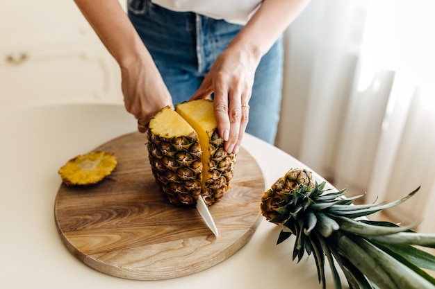 Woman cutting a fresh pineapple on a wooden board