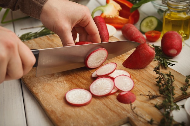 Woman cutting fresh radish on wooden board. Natural eating, preparing healthy dietic vegetable salad at kitchen, closeup