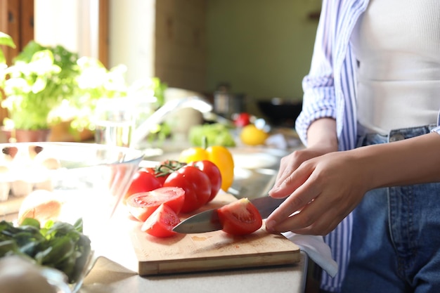 Woman cutting fresh tomatoes at countertop in kitchen closeup
