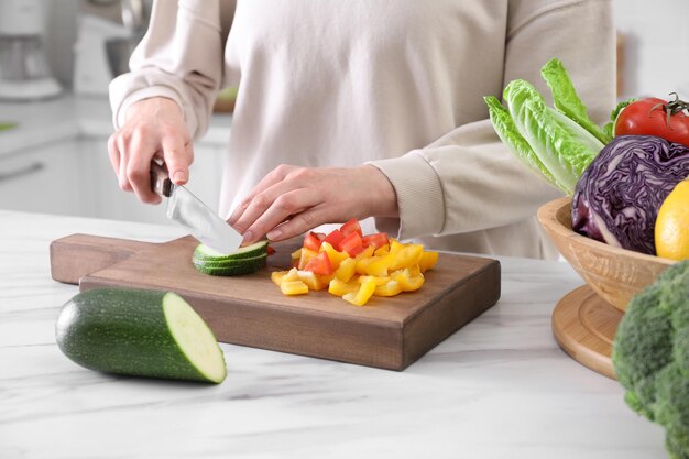 Woman cutting fresh vegetables at table in kitchen closeup