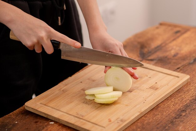 woman cutting onions with knife on wooden background