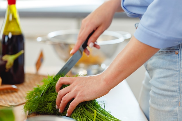 Woman cutting parsley on wooden board in kitchen