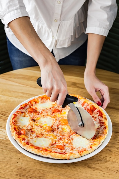Foto pizza di taglio della donna con una taglierina della pizza
