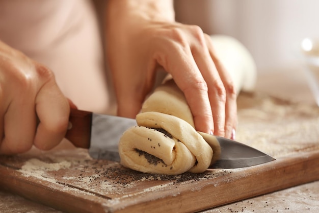 Woman cutting roll with poppy seeds on wooden board in kitchen