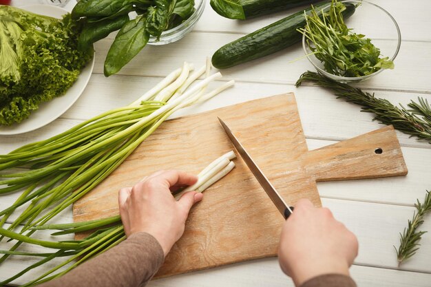 Woman cutting spring onion on wooden board for salad. Preparing organic food, natural homemade eating, top view, copy space