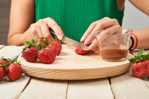 Foto donna che taglia alcune fragole per prenderle immerse nel cioccolato.