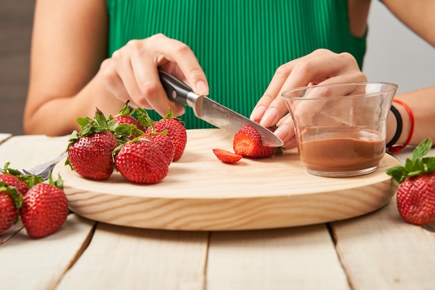 Woman cutting up some strawberries to take them dipped in chocolate.