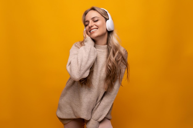 Woman dancing to music in white headphones on yellow background