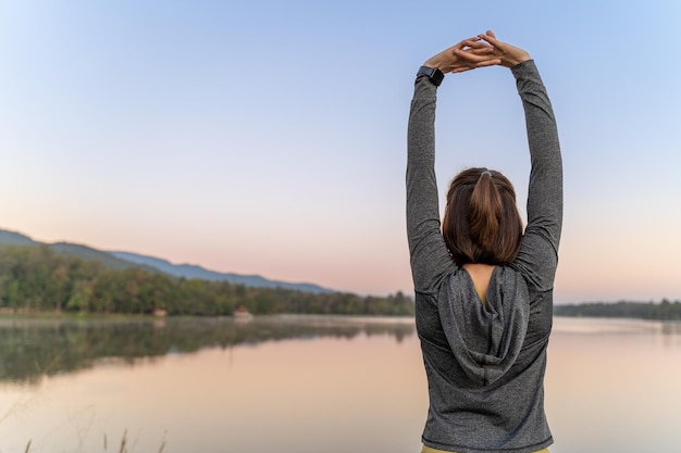 Woman in dark jacket stretching her arms during her break from her morning exercise at a local lake