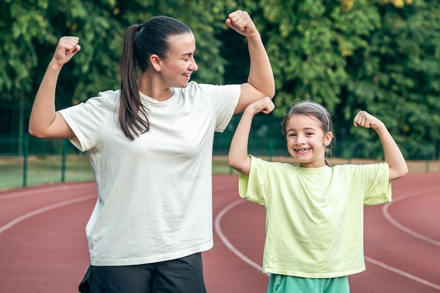 A woman and daughter are showing their biceps working out at the stadium