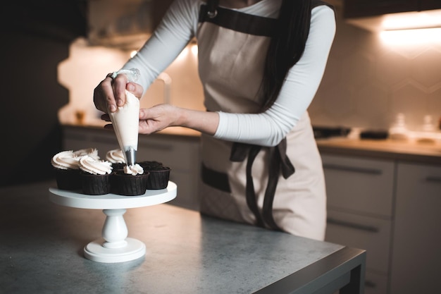 Woman decorate chocolate muffins with whipped cream cheese in kitchen