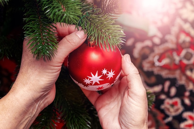 A woman decorates a Christmas and New Year tree A New Year's ball in the hands of a woman near a Christmas tree