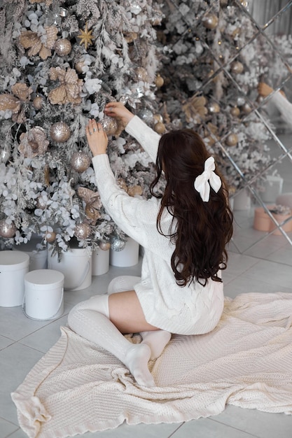Женщина украшает елку гирляндами и игрушками дома подарки под елкой Утро перед Рождеством Новый год 2023