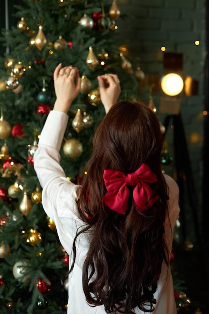 Woman decorates a Christmas tree with garlands and toys at home Morning before Christmas New Year 2023