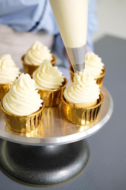 A woman decorates cupcakes from a pastry bag with cream. No face, close up. bright kitchen.