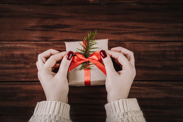 Женщина украшает подарочную коробку красной лентой. Упаковка рождественских подарков.