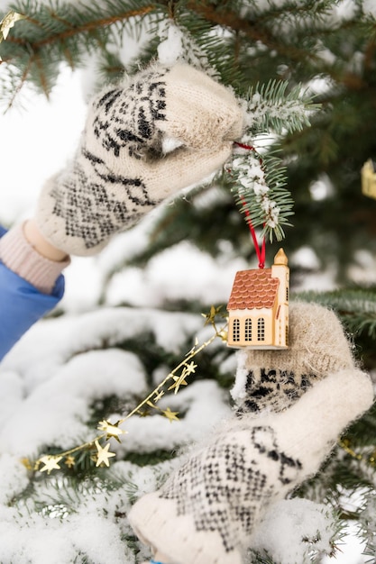 Woman decorating Christmas tree outdoors. Closeup of hands in mittens with Christmas decor