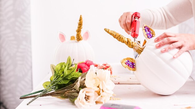 Woman decorating craft pumpkin with unicorn theme for Halloween.