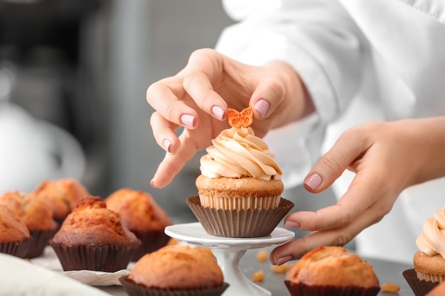 Woman decorating tasty cupcake at table