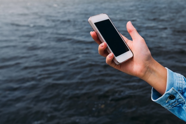 The woman in a denim jacket holds the mobile phone in her hand on